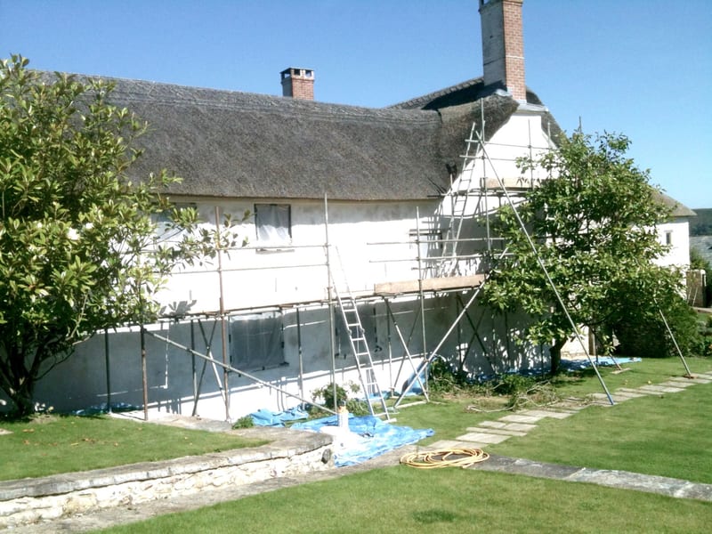 Thatched cottage undergoing lime wash restoration with scaffolding